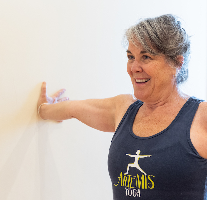 woman smiling with hand at wall doing yoga pose that stretches wrist