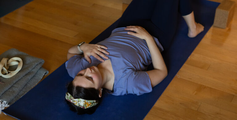 Woman lying on yoga mat in constructive rest pose practicing breath work